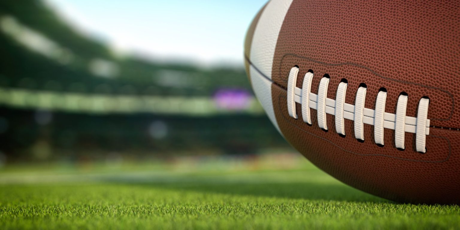 American football ball on grass of football arena